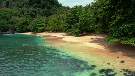 Drone-flyover-empty-beach-with-turquoise-colored-water-in-lush-forest-of-Principe-Island