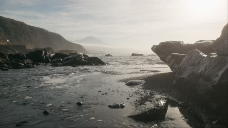 ätherischer-Schwarzer-Sandstrand-Und-Pico-Del-Teide-Berg-In-Der-Ferne,-Neblige-Küste-Mit-Sanften-Wellen-Im-Morgengrauen,-Teneriffa-Kanarische-Inseln,-Vertikale-Schwenk