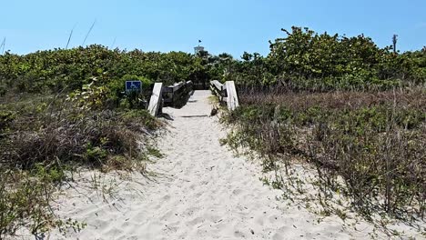 Walking-through-sand-towards-handicap-wooden-beach-bridge,-cocoa-beach-Florida