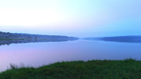 Morning-calm-lake-,-before-sun-lake-reflecting-the-atmospheric-effects-of-the-sky-and-surrounded-by-misty-fogs