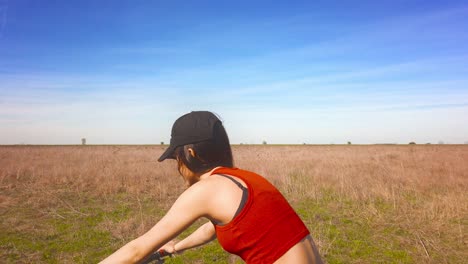 A-girl-is-riding-a-bicycle-through-a-spring-meadow,-surrounded-by-lush-green-grass-and-blooming-flowers