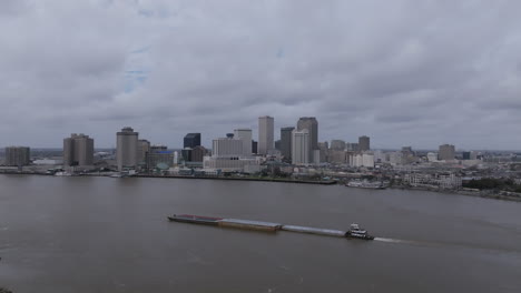 Aerial-footage-flying-backwards-away-from-a-large-barge-that-is-sailing-up-the-Mississippi-River-with-downtown-New-Orleans-in-the-background