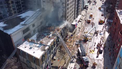 Aerial-view-over-firefighters-attending-to-multiple-building-fire-with-smoke-rising-from-rooftop,-Montreal