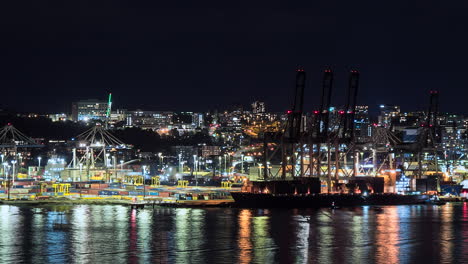 Auckland,-New-Zealand-port-nighttime-time-lapse-with-lights-reflecting-off-the-water-as-straddle-carriers-stack-shipping-containers