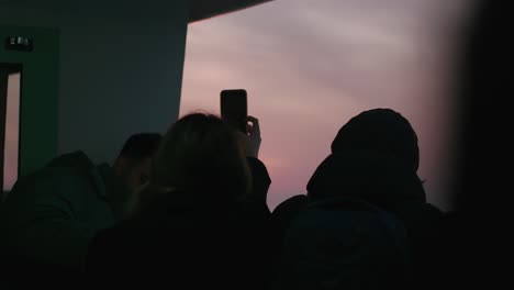 Crowd-on-a-boat-captivated-by-a-vibrant-sunset,-person-filming-on-phone,-returning-from-Burano-island,-Venice