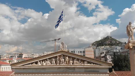 Scenic-aerial-shot-flying-over-the-top-of-the-Akademy-of-Athens-in-Panepistimio,-with-Lycabettus-hill-in-the-background