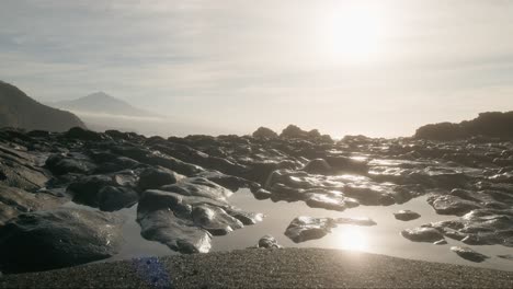 Morning-beach-black-sand-rocks-and-sun-reflection-in-tide-pools,-Playa-de-la-Arena-Tenerife-Canary-Island,-vertical-pan