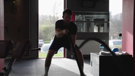 Dark-masculine-male-silhouette-at-indoor-gym-perform-battle-rope-exercise