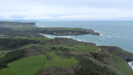 Luftaufnahme-Der-Stadt-La-Sorrozuela-Und-Des-Strandes-La-Arena-Mit-Blick-Durch-Grüne-Hügel-Vom-Kap-Quejo,-Kantabrien