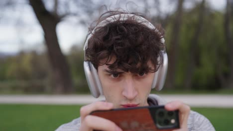 Concentrated-male-with-wireless-headphones-enthusiastically-play-games-on-phone