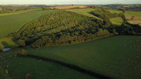 Drone-flies-over-farmland-in-Cornwall,-UK-at-sunset