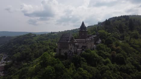 Medieval-Stahleck-Castle-atop-Lush-Hill-overlooking-Bacharach-Town-and-Rhine-Valley,-Drone-Reveal