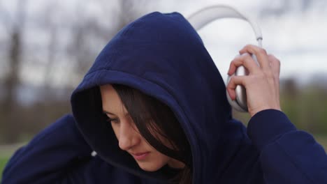 Caucasian-woman-in-blue-hoodie-use-silver-wireless-headphones-at-outdoor-park