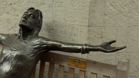 Statue-of-John-Lennon-on-a-bench,-Imagine,-Carnaby-Street,-London,-Day,-People-walk-past,-Medium-Shot,-Side-Angle