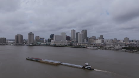 Static-aerial-video-of-a-large-barge-that-is-sailing-up-the-Mississippi-River-with-downtown-New-Orleans-in-the-background