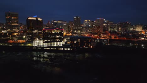 Vista-Aérea-Nocturna-Del-Horizonte-De-Richmond,-Va,-Con-Edificios-Iluminados-Y-Frente-Al-Río-Oscuro