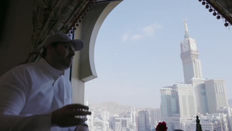 Hombre-Bebiendo-Y-Conversando-En-Un-Restaurante-Con-Vistas-A-Las-Torres-Del-Reloj-En-La-Meca,-Arabia-Saudita