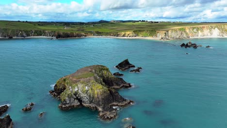Drone-static-seascape-small-islands-and-deep-blue-seas-deserted-beaches-and-sea-cliffs-with-clouds-on-a-spring-day-ar-the-Waterford-Coast-in-Ireland-establishing-shot