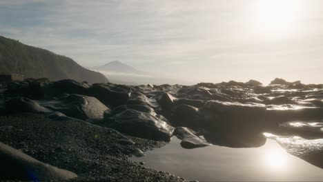 Etérea-Playa-De-Tenerife-Al-Amanecer-Con-Arena-Negra-Y-Roca-Volcánica-Y-El-Brumoso-Pico-Del-Teide-Al-Fondo,-Playa-De-La-Arena-Islas-Canarias