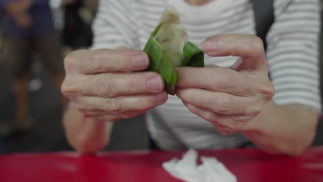 Fish-cake-wrap-banana-leaves-southeast-asian-snack-closeup-hands-unfold-snack