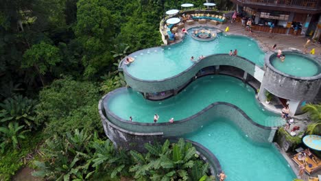 People-relaxing-at-Multi-layer-infinity-pool-of-Cretya-jungle-club-in-Alas-Harum,-Drone-Shot