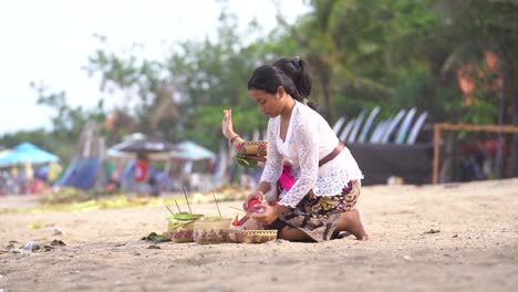 two-women-praying-on-Kuta-beach,-making-offerings-to-the-gods-in-Hinduism