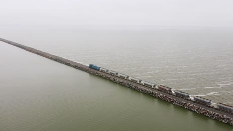 Long-industrial-freight-train-on-straight-track-by-sea-in-Argentina,-aerial-pan
