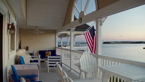 Die-Amerikanische-Flagge-Weht-Bei-Sonnenuntergang-In-Zeitlupe-Auf-Der-Veranda-Der-Stadt