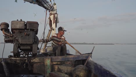 A-traditional-fisherman-skillfully-casts-his-fishing-net-using-bamboo-from-his-old-boat-powered-by-an-old-motor-engine,-as-seagulls-soar-gracefully-overhead,-Creating-a-beautiful-scene