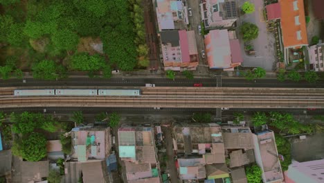 An-overhead-perspective-of-Bangkok's-city-railway,-with-a-train-traversing-its-tracks-amidst-the-surrounding-settlement,-capturing-the-essence-of-urban-connectivity-and-bustling-infrastructure