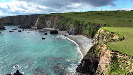 Drone-Estableciendo-Una-Toma-De-La-Costa-Con-Un-Mar-Verde-Esmeralda-Y-Exuberantes-Tierras-De-Cultivo-En-Waterford,-Irlanda,-En-Una-Tarde-De-Primavera