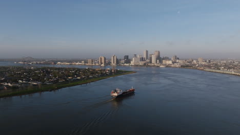 Static-aerial-footage-of-a-barge-on-the-Mississippi-River-moving-towards-the-financial-district-of-downtown-New-Orleans,-Louisiana