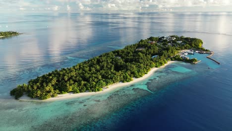 Drone-footage-slowly-panning-around-the-local-island-of-Thinadhoo-early-in-the-morning,-with-clear-blue-waters-in-the-Maldives