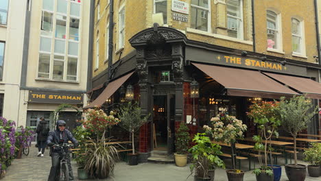 Man-pulls-down-awning-at-The-Starman-pub,-bike-courier-passes-by,-Heddon-Street,-London,-Day