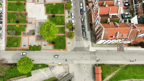 Aerial-view-of-a-cityscape,-featuring-a-crossroads-with-cars,-a-pedestrian-area-with-benches-and-green-trees,-surrounding-residential-buildings,-and-distinct-architectural-elements