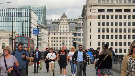 Toma-En-Movimiento-De-Peatones-Caminando-Por-El-Puente-De-Londres-Durante-El-Día,-Con-Edificios-Emblemáticos-De-La-Ciudad-Al-Fondo-Y-Vehículos-Pasando