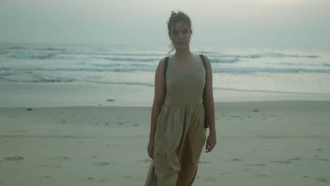 Young-woman-is-walking-on-the-beach-wearing-a-dress-and-a-handbag