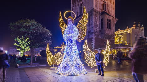 Timelapse-of-crowded-Main-Market-Square-with-Cloth-Hall-,-in-Krakow-at-night-during-Christmas-time-in-winter,-Poland---zoom-in-to-illuminated-angel-statue