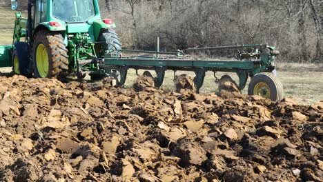 Green-agricultural-tractor-towing-a-plow-to-turn-over-a-field-in-early-spring-in-the-Midwest