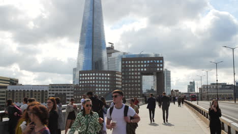 Commuters-of-difference-ethnicity-on-London-Bridge,-backdrop-adorned-by-the-iconic-Shard-building,-under-a-sky-painted-with-billowing-clouds