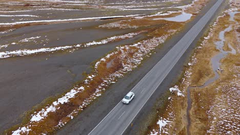 Aerial-Drone-follow-Car-driving-by-Iceland-speedway-snowy-mountains-background