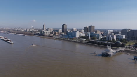 Wide-aerial-footage-of-downtown-Baton-Rouge-over-the-Mississippi-River-with-a-tug-boat-sailing-towards-a-group-of-barges