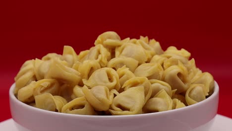 Rohe-Tortellini-Rotieren-Auf-Drehteller-Auf-Rotem-Hintergrund