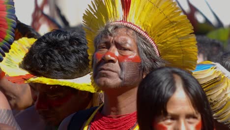 Elder-Indigenous-Amazonian-Leader-in-Headdress-Amongst-Tribal-Members,-Slow-Motion