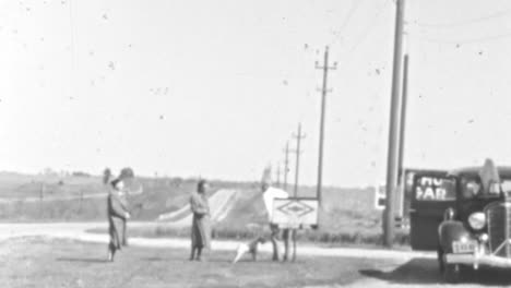 Mujeres-Y-Hombres-Parados-Junto-A-Un-Perro-En-Un-Lugar-Al-Aire-Libre-Al-Borde-De-La-Carretera-En-La-Década-De-1930