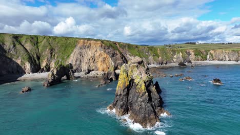 Drones-Rodeando-Pilas-De-Mar-Irregulares-Con-Olas-Espectaculares-Formaciones-Rocosas-Y-Cuevas-Marinas-En-El-Promontorio-De-La-Costa-De-Waterford,-Irlanda,-Una-Naturaleza-Impresionante-En-Una-Ubicación-Impresionante