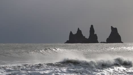 Waves-coming-onto-shore-at-Reynisfjara-Black-Sand-Beach-with-large-basalt-stacks-in-the-background