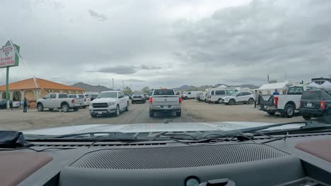 POV---Driving-around-pedestrians-and-vehicles-to-find-parking-near-the-big-tent-for-Sports,-Vacation-and-RV-Show-with-a-million-attendees,-on-rainy-day
