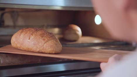 Baker-takes-freshly-baked-bread-loaf-out-of-the-oven-with-peel-in-slow-motion