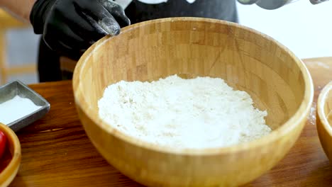Chef-pouring-olive-oil-on-flour-in-a-bowl,-close-up-slow-motion